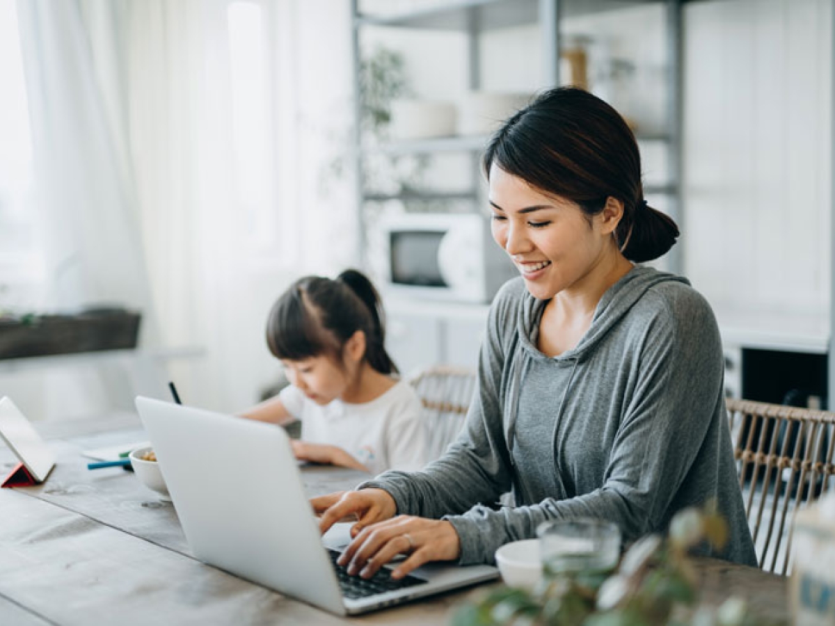 Woman sitting at the table on her computer with her daughter sitting next to her