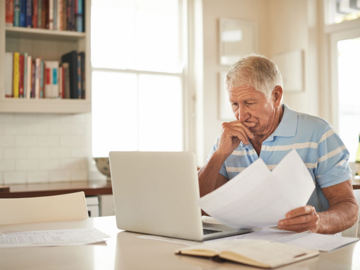 Elderly man concentrating on his paperwork and sitting in front of his laptop Elderly man concentrating on his paperwork and sitting in front of his laptop