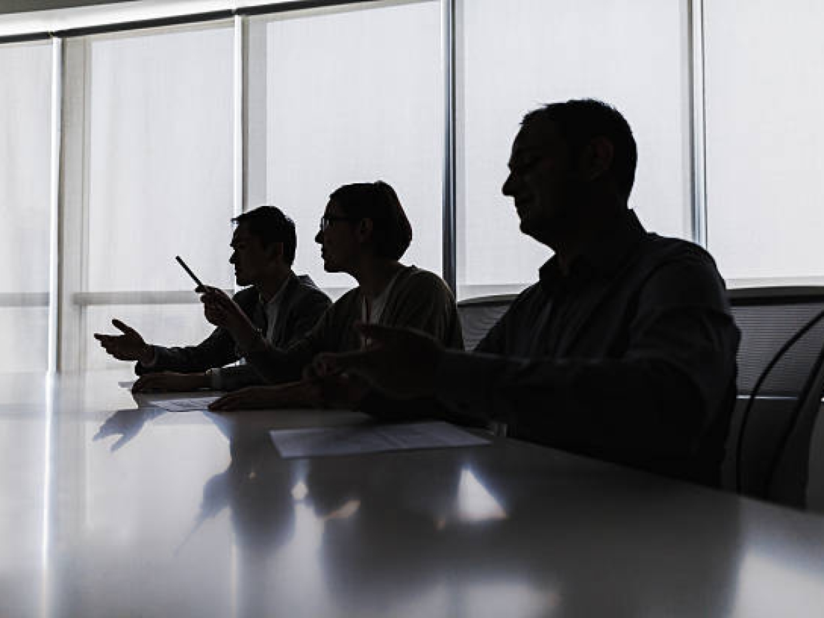 Silhouettes of three people sitting at a boardroom table